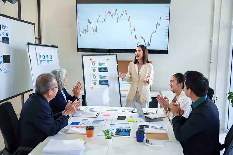Asian businesswoman leading meeting and presenting charts to colleagues clapping