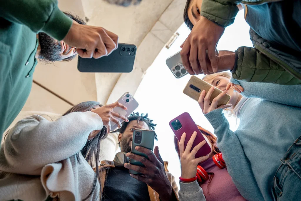 A group of diverse young friends using their smartphones in a circle, seen from a low angle view.