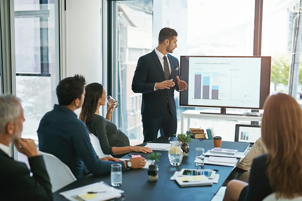 Business man, presentation and monitor in office with group for b2b strategy, speech and graphs. Person, speaker and information on whiteboard, screen and sales with meeting for brand communication